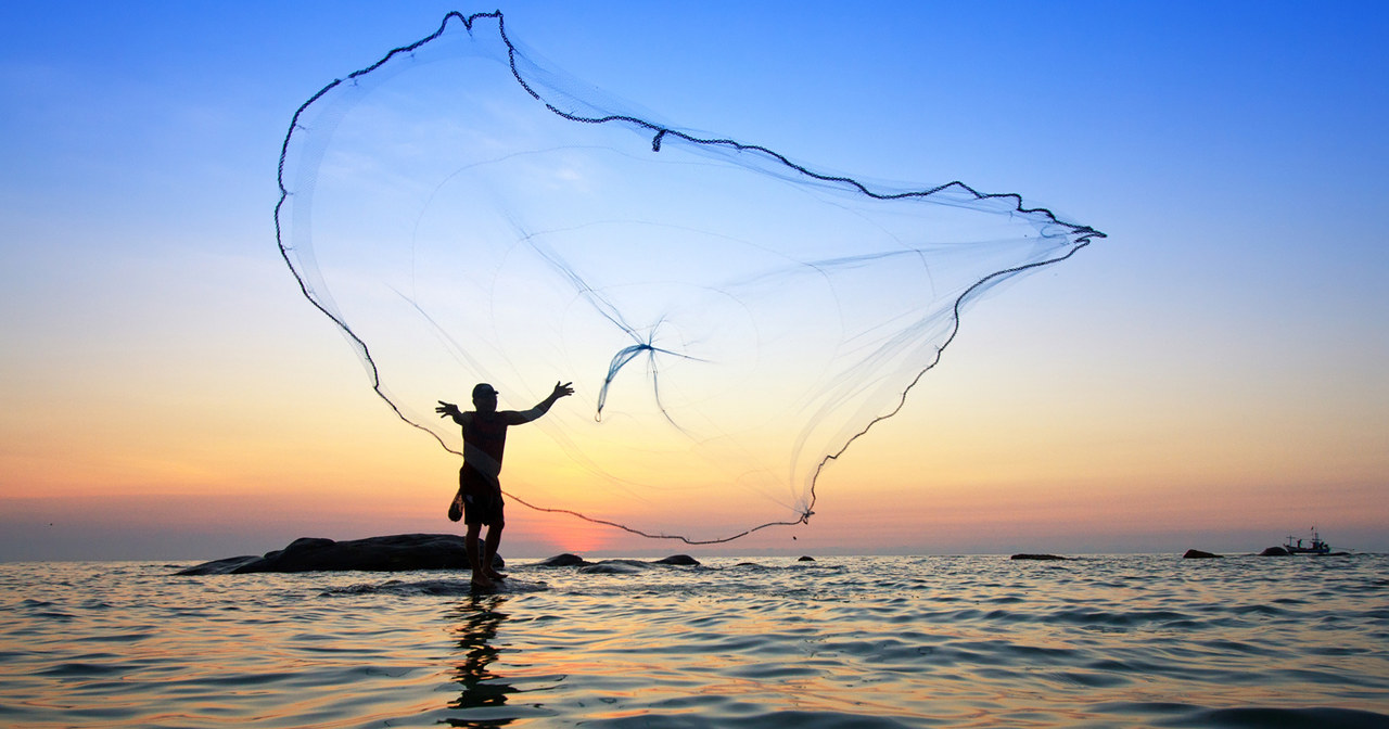 Ein Mann wirft ein großes Netz ins Wasser.