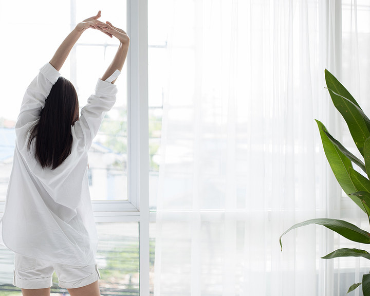 Frau macht Dehn-Übungen vor einem Fenster