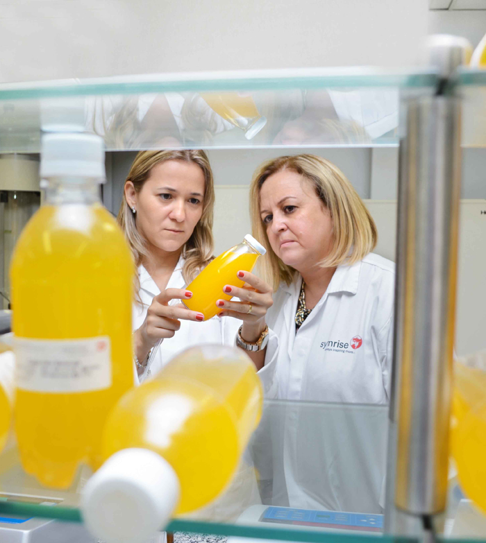 2 women in a laboratory inspecting orange juice