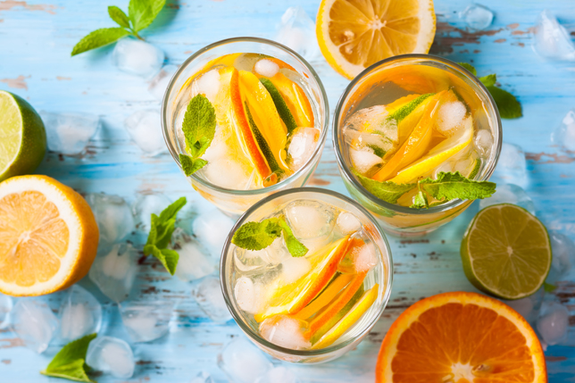 Several glasses of fruit, ice and liquid on a blue table.