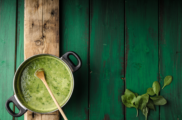 Ein Kochtopf mit einer grünen Suppe und einem Kochlöffel auf einem grünen Untergrund.