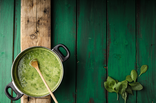 A cooking pot with a green soup and a cooking spoon on a green ground.