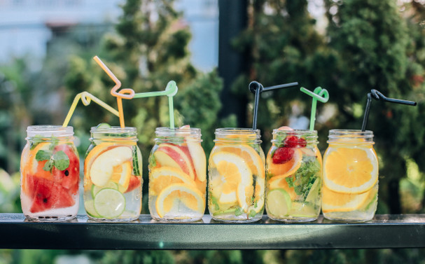 Six glasses with fruits, juice and straws are placed on a counter.