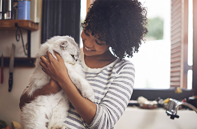 Eine junge Frau hält eine Katze im Arm und lächelt.