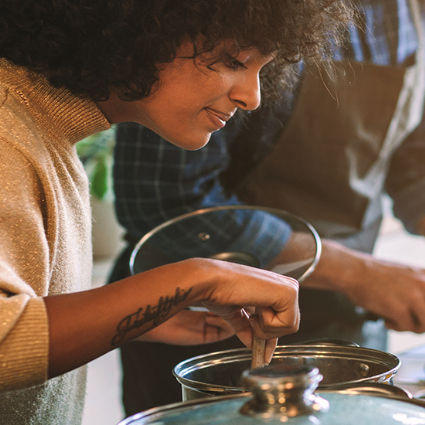 A young woman is stirring a pot with a wooden spoon.