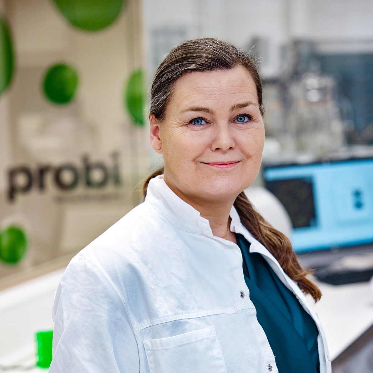 Porträt einer weiblichen Laborfachkraft im weißen Kittel vor Laborgeräten, erstellt für Kommunikation zu probiotischer Forschung