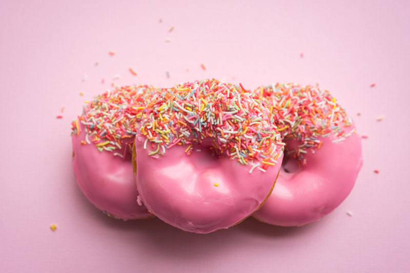 Three pink donuts with colorful sprinkles on a pink ground.