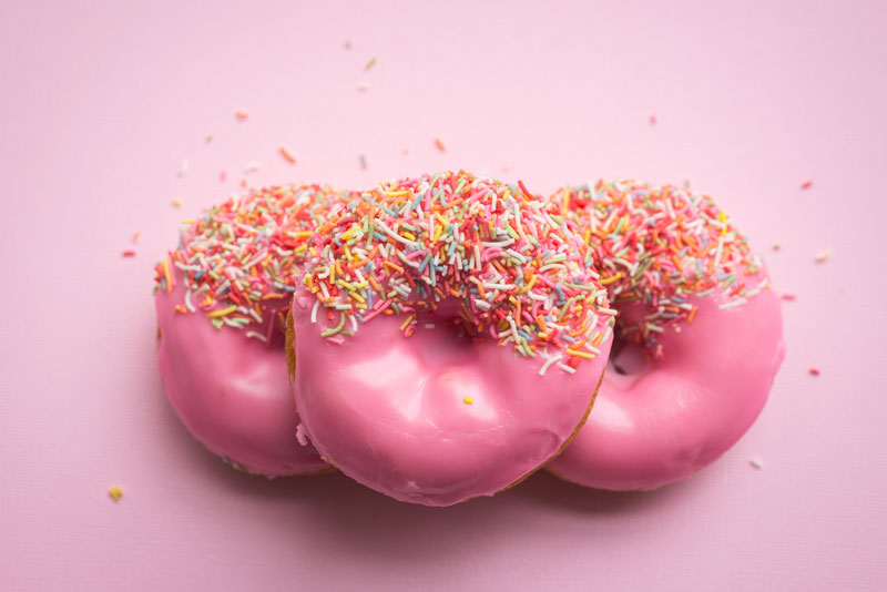 Drei pinke Donuts mit bunten Streuseln auf einem pinken Untergrund.