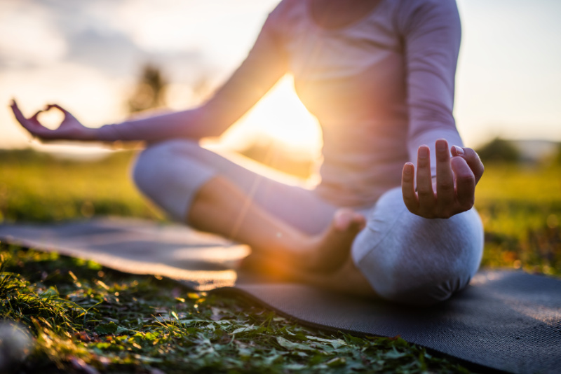 A woman meditates on a field at sunrise.