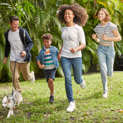 Zwei junge Erwachsene und zwei Kinder laufen mit ihrem Hund auf einer Wiese.